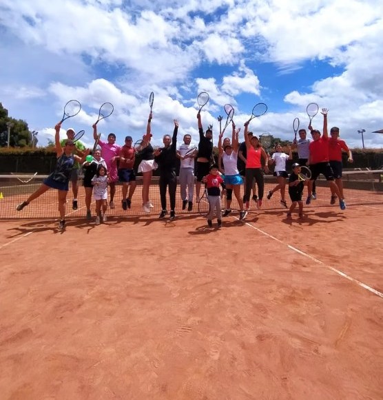 Alumnos y profesores de la escuela saltando con las raquetas en alto en la cancha de arcilla